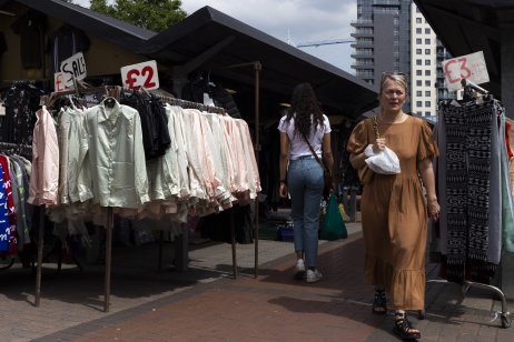 Two shoppers pass by a rack of clothes at a market
