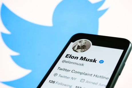 Elon Musk's Twitter account displayed on a phone screen and Twitter logo displayed on a laptop screen