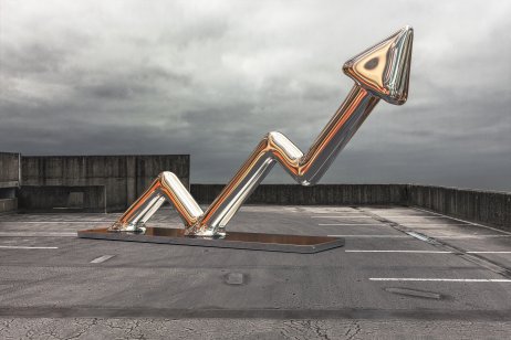 A shiney arrow made from chrome or steel sits on a car park pointing upwards