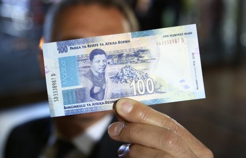 A man holds a new South African banknote at the value of one hundred South African Rand