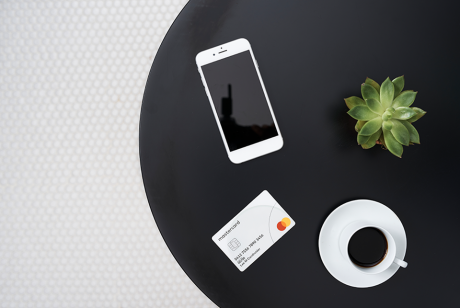 Top-down view of a Mastercard credit card, smartphone, cup of coffee and a plant on a table 