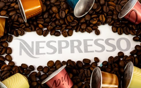 A picture of a Nespresso logo surrounded by coffee beans and coffee capsules, white background with grey text