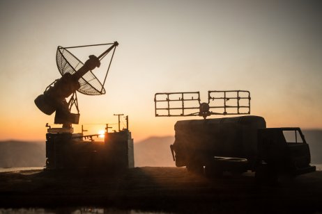 Creative artwork decoration. Silhouette of mobile air defence truck with radar antenna during sunset. 