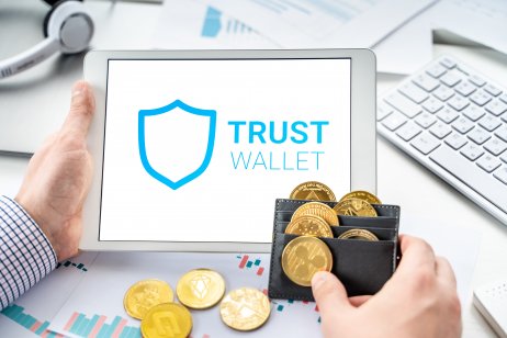 Trust Wal;l;et Token logo on screen with gold cryptocurrency coins in wallet