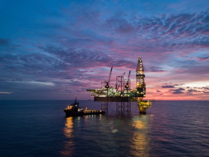A ship is moored beside an oil rig at sunset