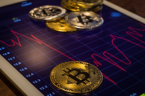 Bitcoins on modern tablet screen that shows red price graph