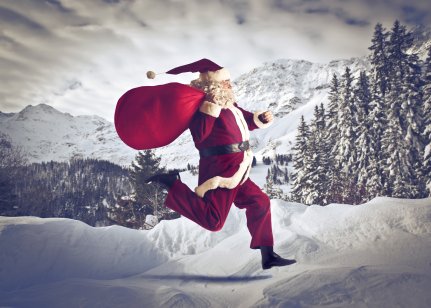 A person dressed like Santa Claus running outside in the snow with trees in the background