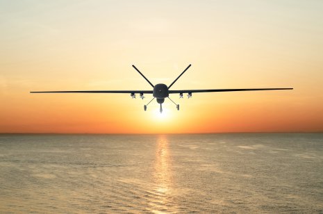 A military drone flies above the sea amid a sunset