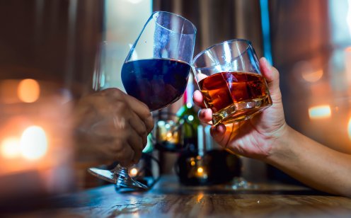 A wine glass and spirit glass are clinked together in a toast