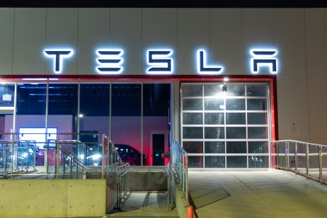 Tesla logo atop of a Tesla Dealership illuminated at night.