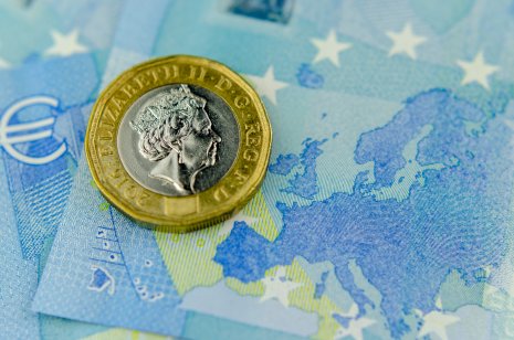 One pound coin on top of 20 Euros banknote, next to a map of the EU