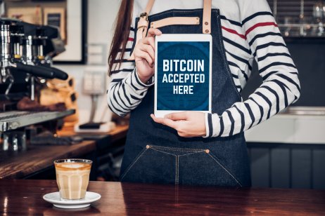 woman barista holding tablet and show bitcoin accepted here on tablet screen at cafe 