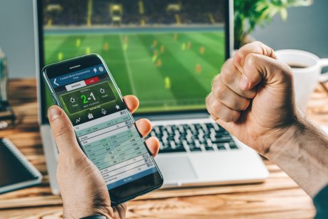 A football support watches a game online while checking a mobile betting app