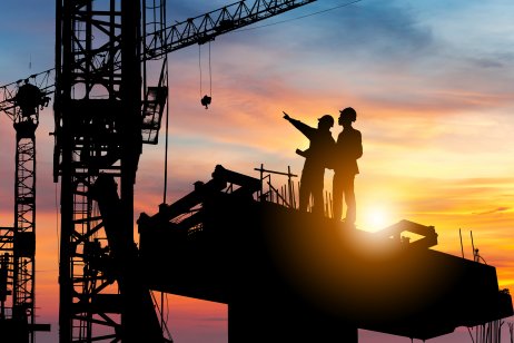 Silhouette of engineer and worker checking project at building site background, construction site at sunset in evening time.