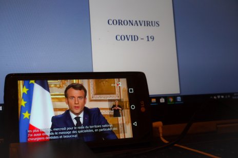 French President Macron speaking via a smartphone with a Covid announcement in front of him 