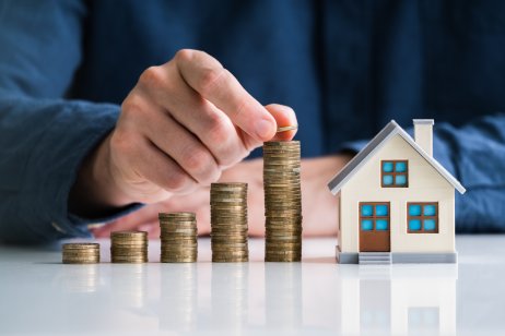 Representation of increasing stacks of coins next to a model house