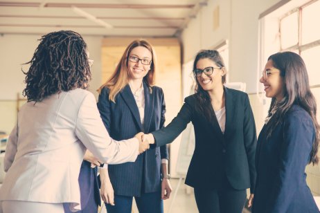 Smiling young businesswomen shaking hands in office. Confident cheerful business partners greeting each other.