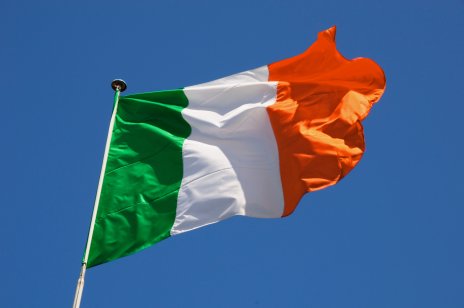 Irish flag fluttering in a brisk breeze against a bright blue sky.