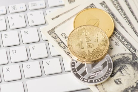 Cryptocurrency tokens sit on top of a stack of dollars placed on a keyboard