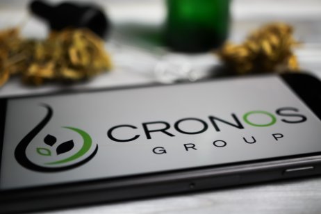 Viersen, Germany - January 9. 2021: Closeup of mobile phone screen with logo lettering of cannabinoid company cronos group, blurred marijuana (focus on letter o in lower lettering)
