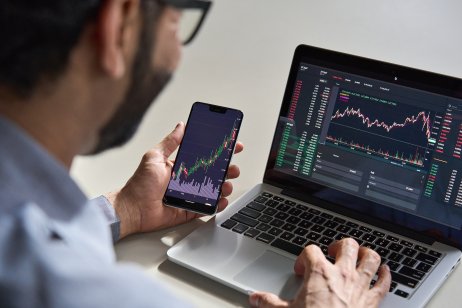 Trader using mobile phone and laptop for trading