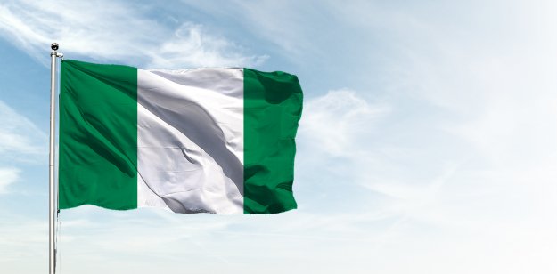 Nigeria flag in the blue sky. Horizontal panoramic banner.