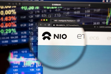NIO stock forecast: Is it time to buy the dip? Nio electric car company logo on a website with blurry stock market developments in the background, seen on a computer screen through a magnifying glass.