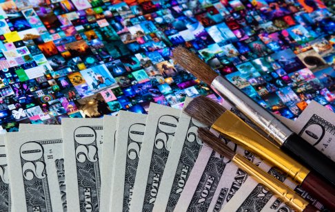 A picture of money with brushes placed on tablet screen showing Beeple NFT art collage Everydays – The First 5000 Days