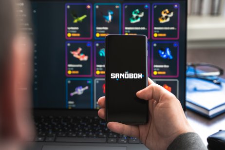 A photo of a hand holding a phone with Sandbox (SAND) logo.