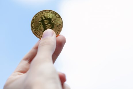 A human hand holding a golden coin with a bitcoin (BTC) logo.