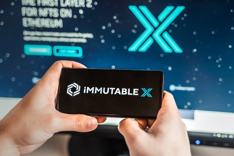 Man playing with crypto coins on a smartphone with the Immutable X logo in the background on a computer screen