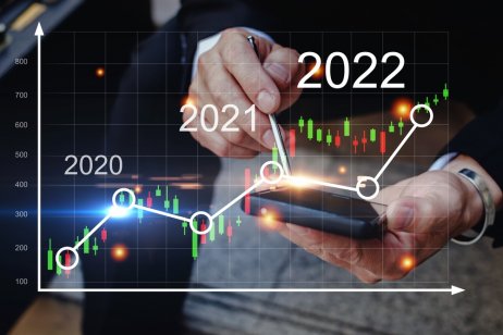 Image of a graph showing rise of markets from 2020 to 2022 with a background of a man's hands using a calculator