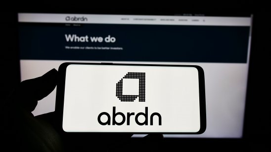 Person holding smartphone with logo of British investment company abrdn plc on screen in front of website. Focus on phone display. Unmodified photo.