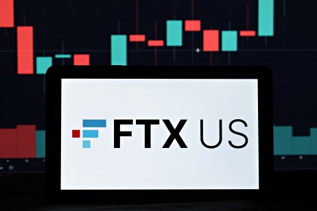 A smartphone displays the FTX.US logo in front a trading chart