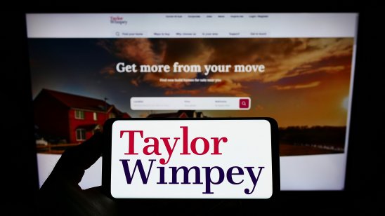 Stuttgart, Germany - 02-26-2022: Person holding smartphone with logo of British housebuilding company Taylor Wimpey plc on screen in front of website. Focus on phone display. Unmodified photo.