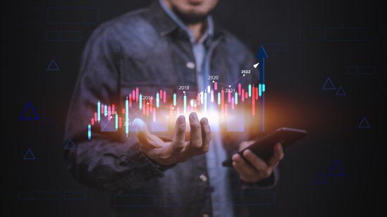 A man holds a holographic candlestick trading chart in his hand next to a smartphone