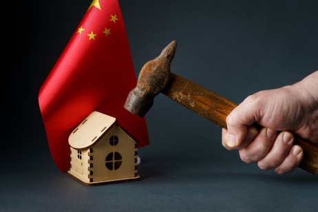 A hammer raised above a toy house with the flag of China in the background.