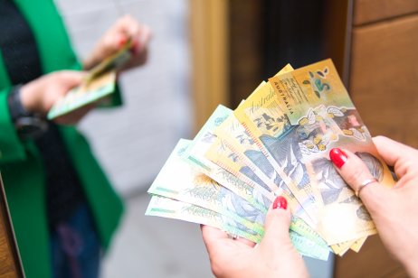 A woman in a green jacket is counting banknotes of Australian dollars.