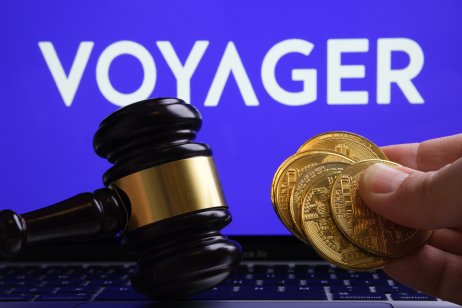 Voyager coins held in a male hand over a computer keyboard. Voyager logo in the background. A gavel on the side symbolising Voyager’s court hearings.