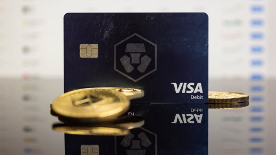Cryptocurrency tokens lie on a table in front of a Crypto.com Visa card