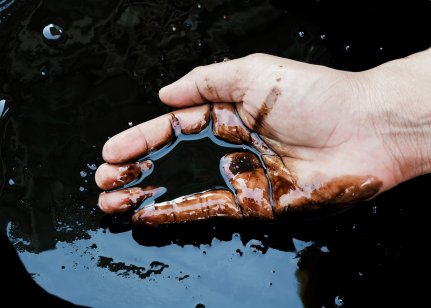 A hand scoops crude oil from a leak