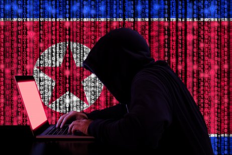 Hacker in a dark hoody sitting in front of a notebook with digital North Korea flag in the background