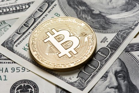 A bitcoin token rests on dollar notes 