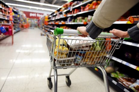 A shopper wheels a full trolley through a supermarket aisle