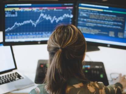 A female trader looking at two screens displaying stock market data.