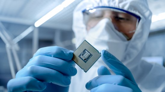 Man in lab gear holding a semiconductor chip