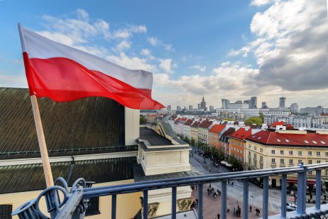 The flag of Poland in the Blue sky and the center of Warsaw in the background