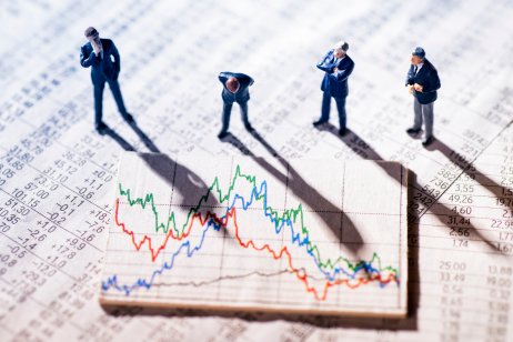 Mini-statues of businessmen observing stock market charts showing volatility 