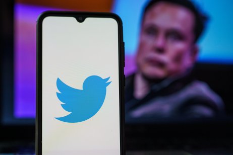 Twitter logo on cell phone with Elon Musk in the background.