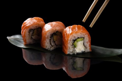 A picture of sushi rolls with chopsticks. Set on a black background with reflection. Sushi roll with rice, cream chees, salmon, avocado.